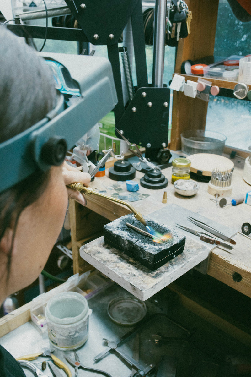 A woman meticulously crafting a unique piece of jewelry in her workshop, showcasing her custom creations